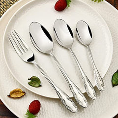 Four-piece cutlery set with patterned handles laid flat on white plate with fruit and leaves.