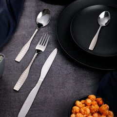 Cutlery set with engraved handles styled beside matte black plates and spicy chickpeas on dark background.