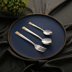 Cutlery trio with gold detailing arranged on a dark blue plate over smooth black satin fabric.