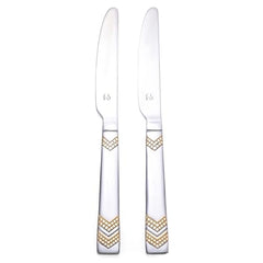 Two stainless steel dinner knives with elegant gold chevron pattern handles standing upright on clean white background for premium flatware display.