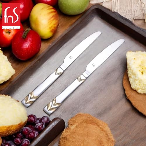 Two Raga stainless steel dinner knives with gold chevron handles on gray tray surrounded by fresh apples, berries, and artisan bread.