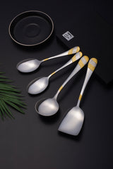 Stylish silver-gold serving utensils arranged on black surface with decorative elements and branded packaging.