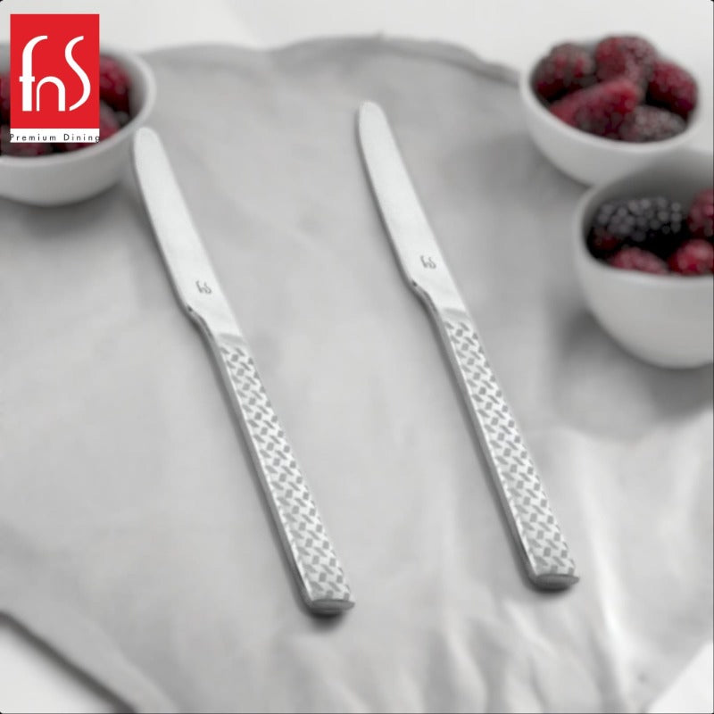 Two FnS Rhombo dinner knives with distinctive geometric diamond-pattern textured handles on white plate beside small bowls with berries.