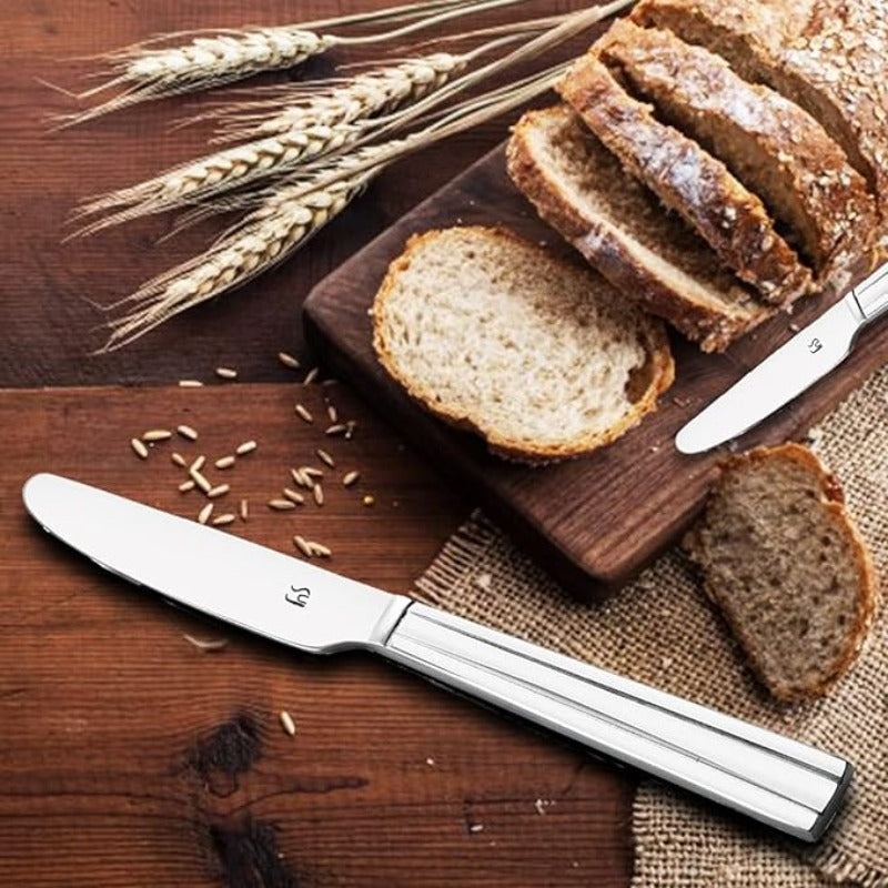Stainless steel dinner knife cutting fresh artisan bread on wooden board with wheat stalks, showcasing sharp blade and elegant tapered handle design.