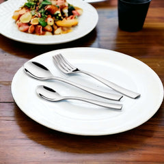 Stainless steel fork and spoons arranged on a white plate with a salad dish in background.