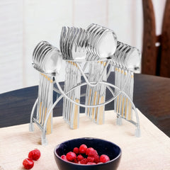 Elegant 24-piece FNS cutlery set with gold-accented handles in stand, placed on dining table.
