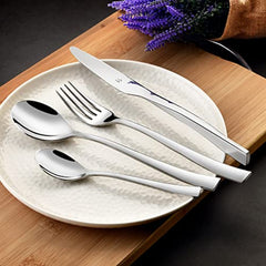 Elegant silver cutlery set with curved handles arranged on textured plate beside lavender on wood board.