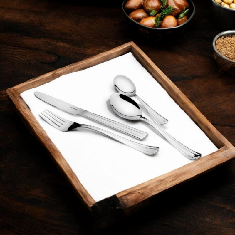 Elegant four-piece cutlery set arranged on a wooden tray beside bowls of nuts and food.