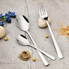 Elegant silver fork and spoons displayed on textured surface, surrounded by decorative items and flowers.
