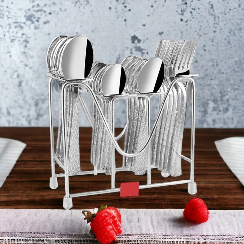 Full cutlery set with patterned handles in metal stand on wooden dining table with raspberries nearby.