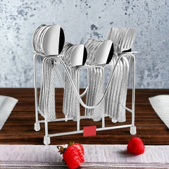 Full cutlery set with patterned handles in metal stand on wooden dining table with raspberries nearby.