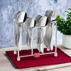 Stainless steel cutlery set neatly arranged in metal stand on red mat, with potted plant nearby.