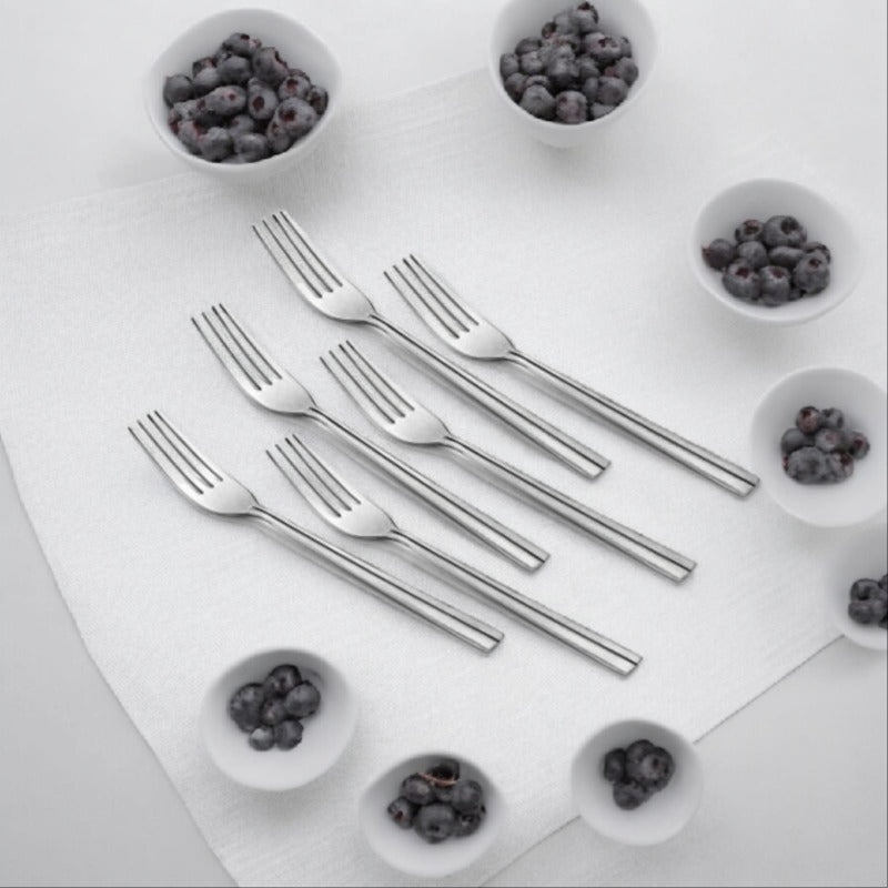 Six stainless steel forks arranged on white cutting board surrounded by small bowls of blueberries