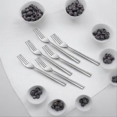 Six stainless steel forks arranged on white cutting board surrounded by small bowls of blueberries