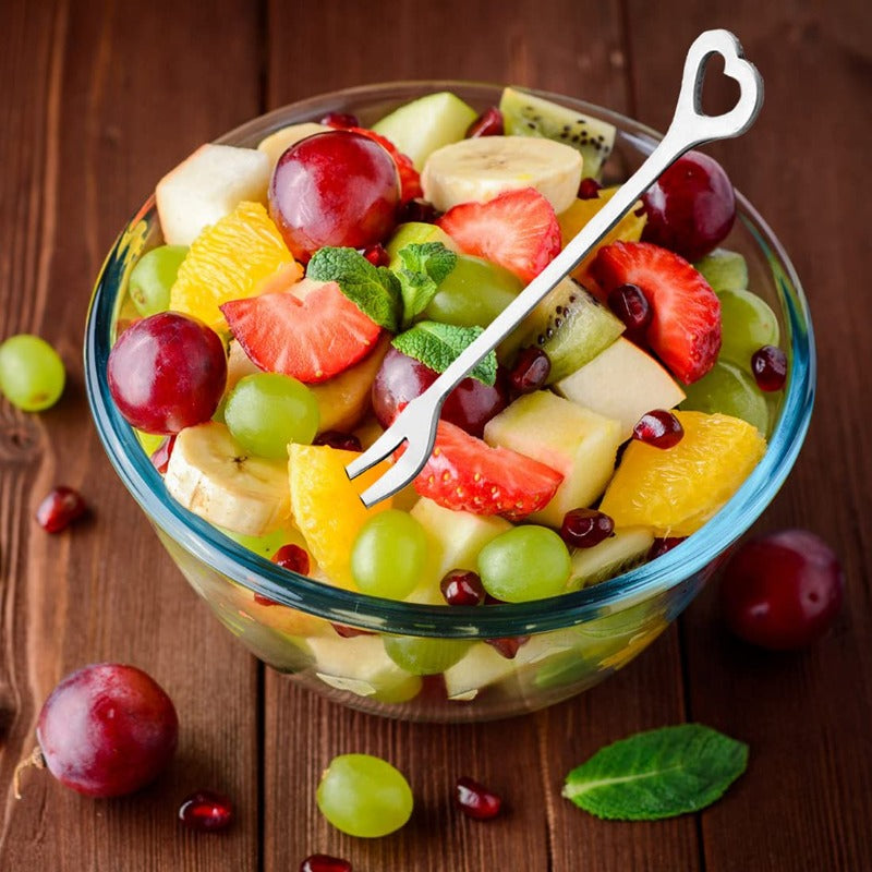 Colorful fruit salad in glass bowl with heart-shaped fork on wooden table