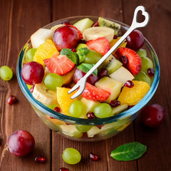 Colorful fruit salad in glass bowl with heart-shaped fork on wooden table