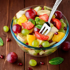 Mixed fruit salad with decorative fork in glass bowl on wood