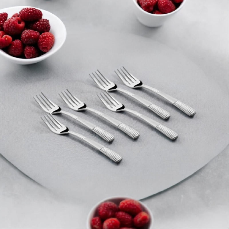 Six stainless steel dinner forks with textured handles arranged on gray surface with raspberry bowls