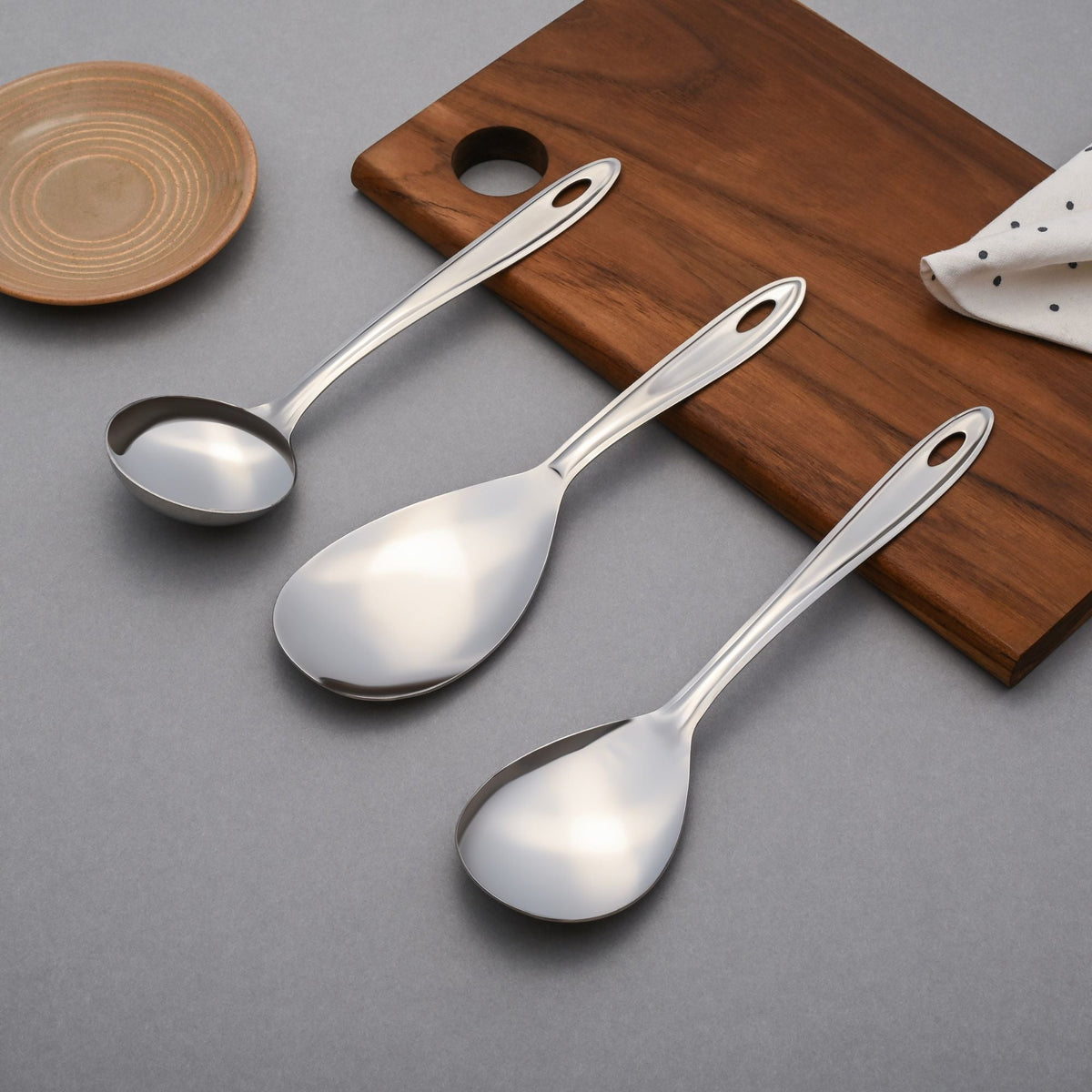 Three trinity stainless steel serving spoons arranged on wooden holder showing different spoon sizes and elegant design aesthetic.