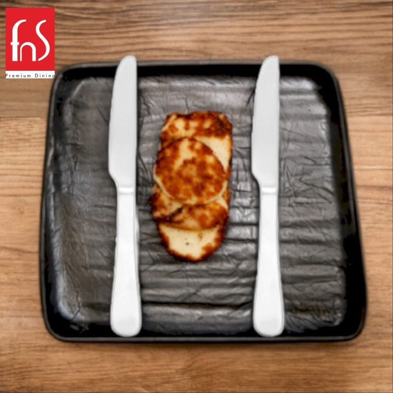 Two stainless steel dinner knives placed on black square plate with grilled halloumi cheese slices on wooden table, branded FnS Premium Dining.