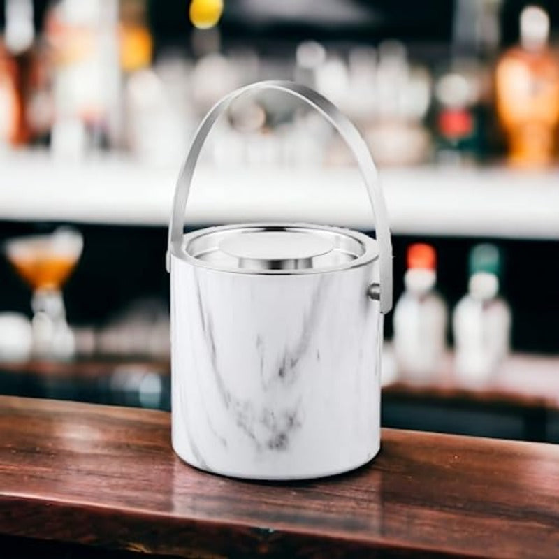White marble pattern ice bucket with stainless steel rim and handle on wooden bar counter with blurred liquor bottles in background